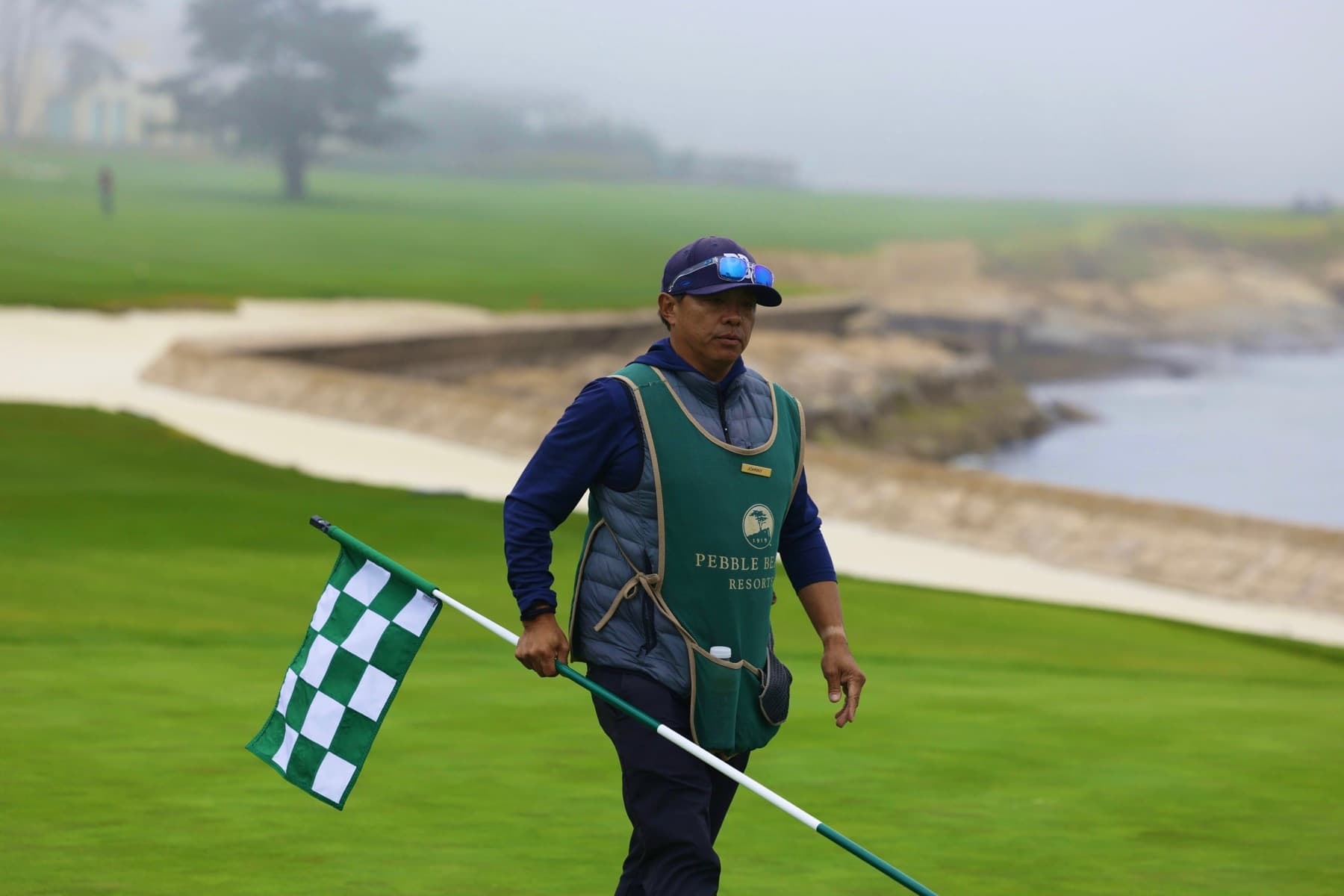 Johnny carrying the flag across a seaside green on a foggy morning