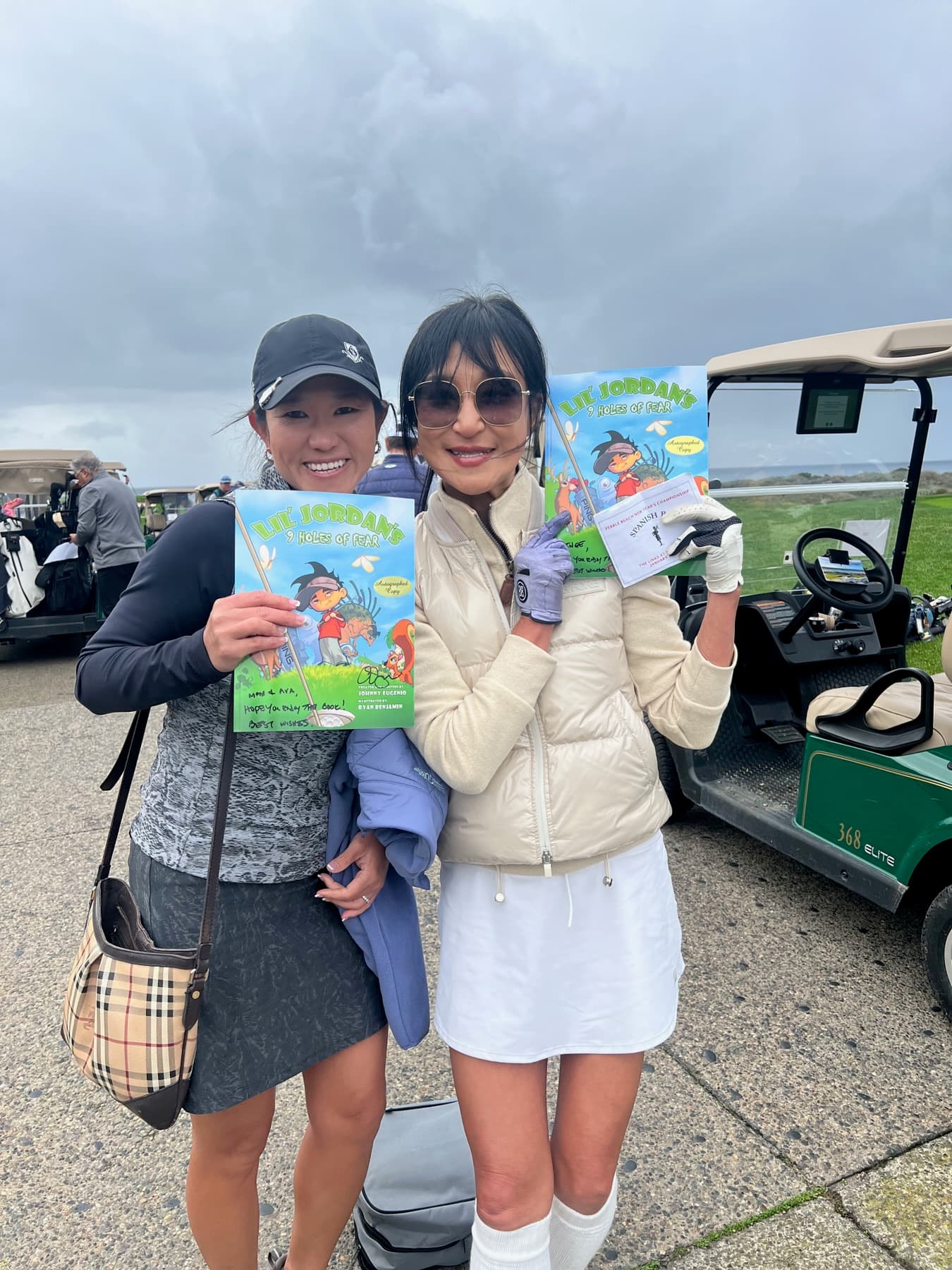 Two golfers holding copies of the book by the carts